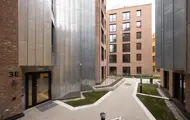 Inngangsparti og felles gårdsrom mellom moderne leilighetsbygg med tegl- og metallfasader.