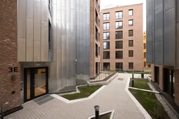 Inngangsparti og felles gårdsrom mellom moderne leilighetsbygg med tegl- og metallfasader.