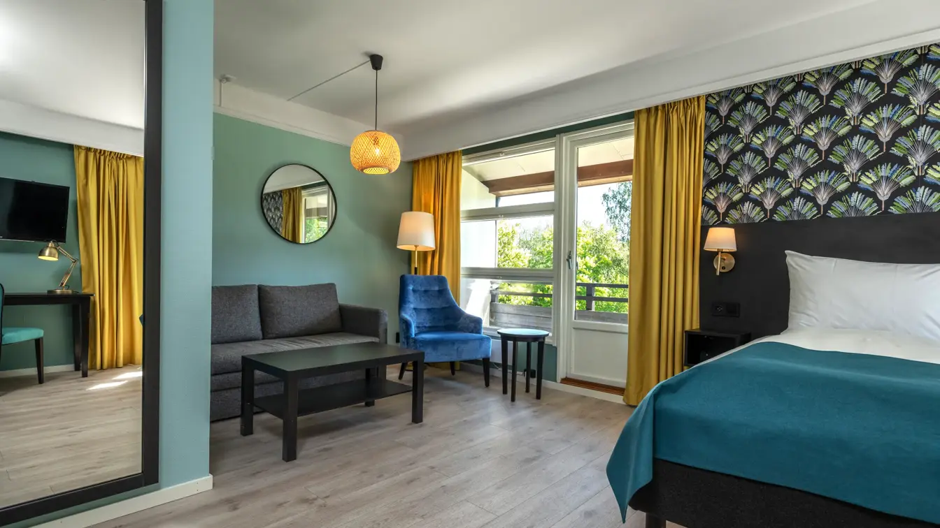 Familierom med dobbeltseng, sovesofa, blå lenestol, gule gardiner, helspeil, parkett, og balkong