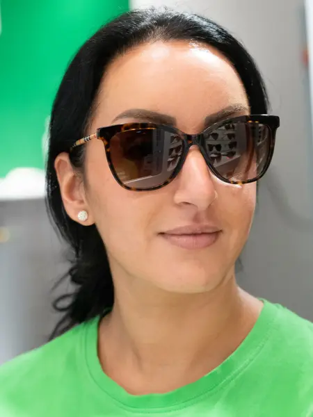 Jente med mørk hår og grønn genser, haar på seg en mørkebrun solbrille fra Burberry