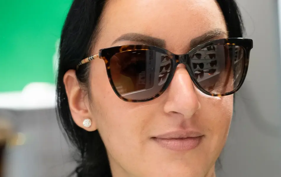 Jente med mørk hår og grønn genser, haar på seg en mørkebrun solbrille fra Burberry