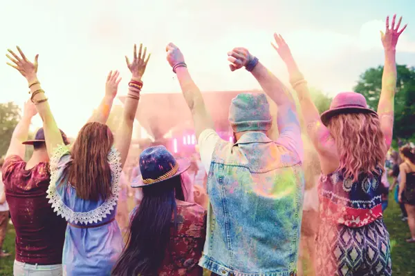 Fire venner står med hendene i været på festival.