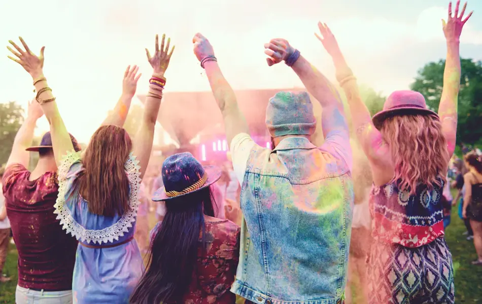 Fire venner står med hendene i været på festival.