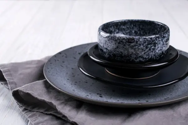 Stack of simple porcelain handmade gray and black plates and  bowls on a white wooden table.