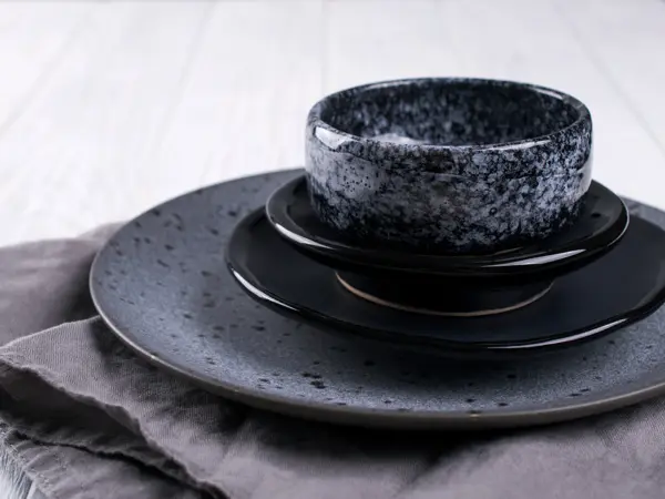 Stack of simple porcelain handmade gray and black plates and  bowls on a white wooden table.