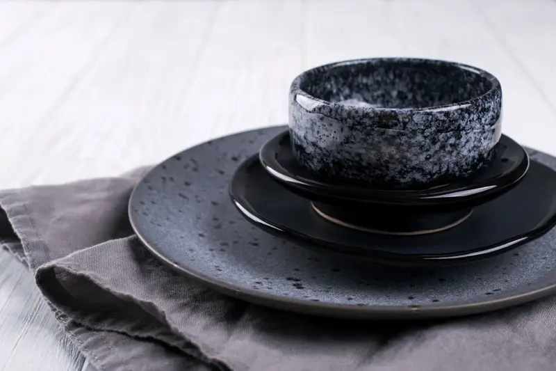 Stack of simple porcelain handmade gray and black plates and  bowls on a white wooden table.