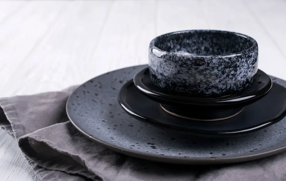 Stack of simple porcelain handmade gray and black plates and  bowls on a white wooden table.