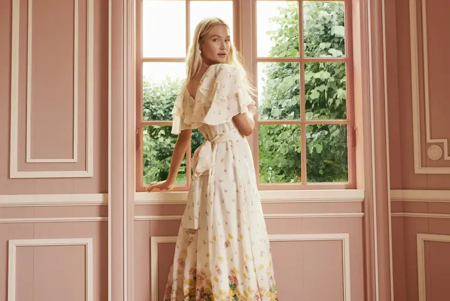 Dame som står ved et vindu og ser på kameraet