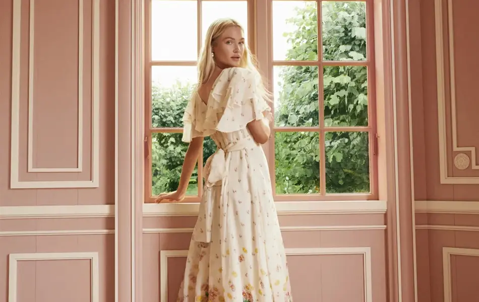 Dame som står ved et vindu og ser på kameraet