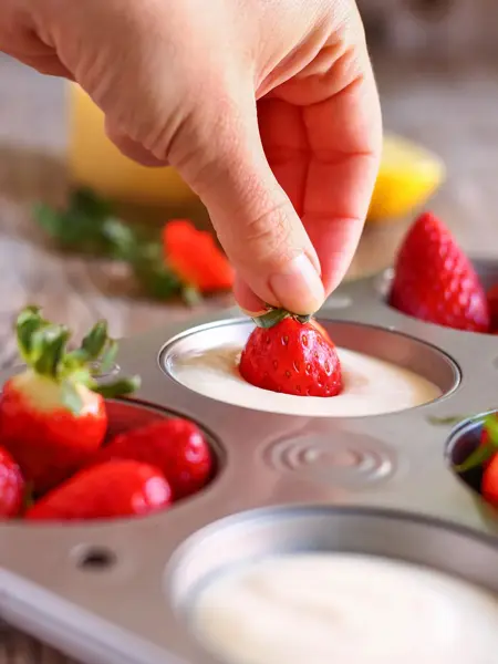 Person dypper jordbær i hvit masse