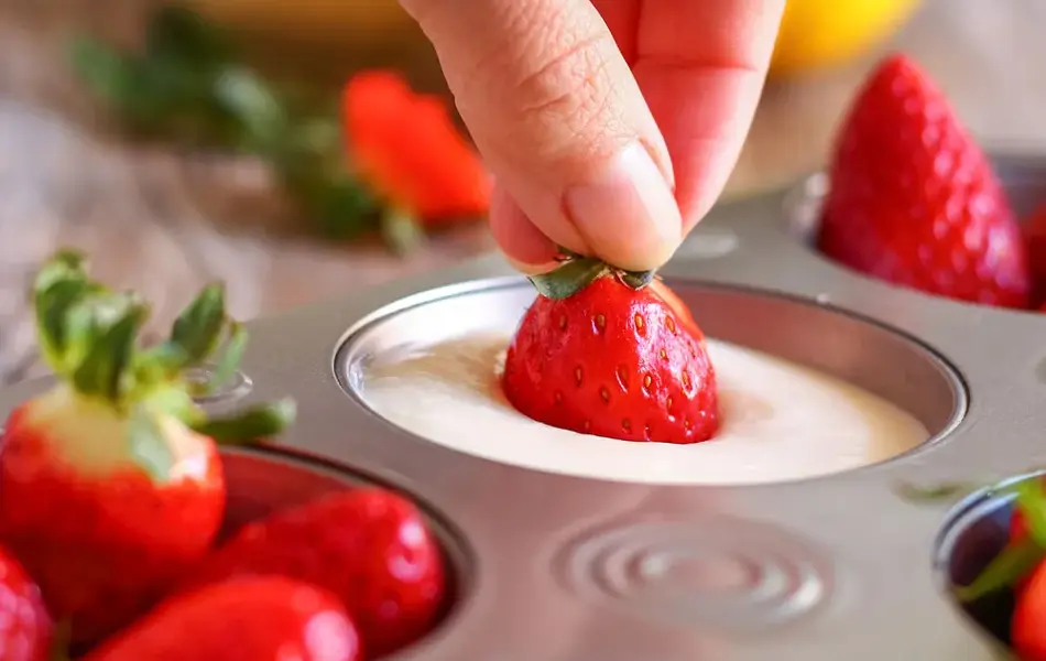 Person dypper jordbær i hvit masse