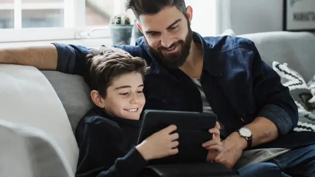 far og sønn i sofa med nettbrett