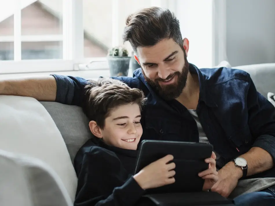 Far sitter med sønn som ser på nettbrett