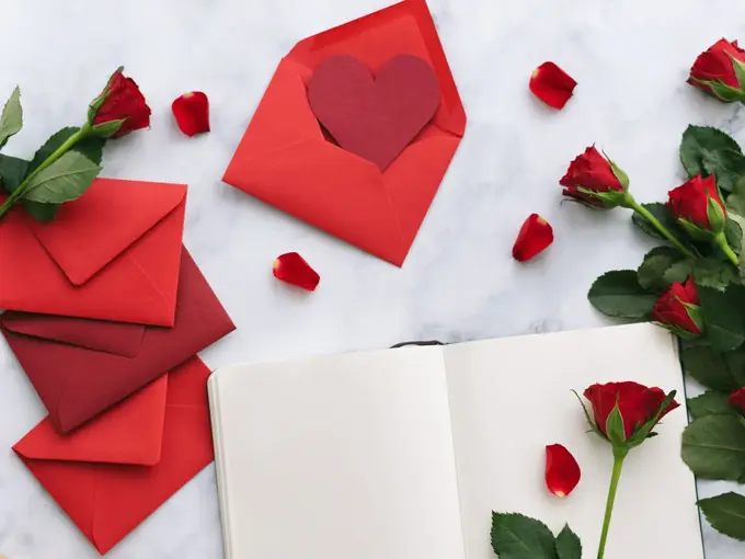 Åpen bok på bord med røde konvolutter og røde roser rundt