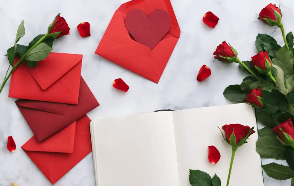 Åpen bok på bord med røde konvolutter og røde roser rundt