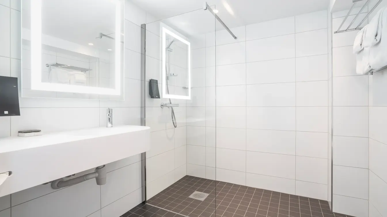Vask, speil med led lys rundt og dusj på bad i business rom på Thon Hotel Bristol Bergen.
