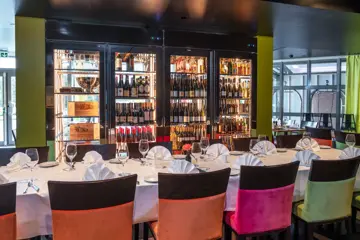 Spisebord dekket med servise, brune stoler og et brunt spisebord. Vinskap med diverse vin i bakgrunn. 