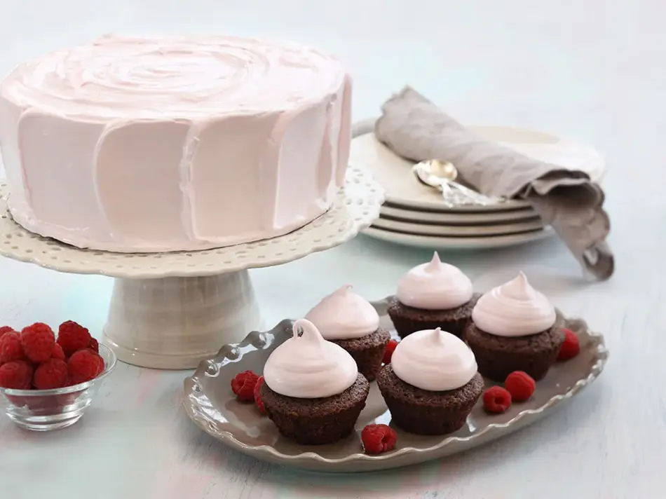 Fem sjokolademuffins med rosa topping ved siden av en rosa kake