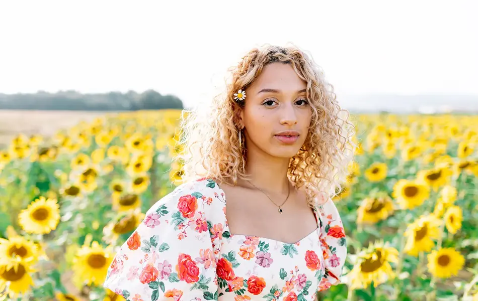 Dame med fargerik blomsterkjole står i blomstereng 