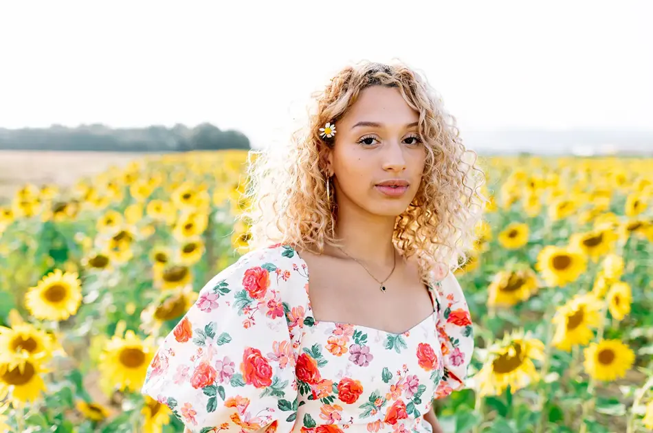 Dame med fargerik blomsterkjole står i blomstereng 