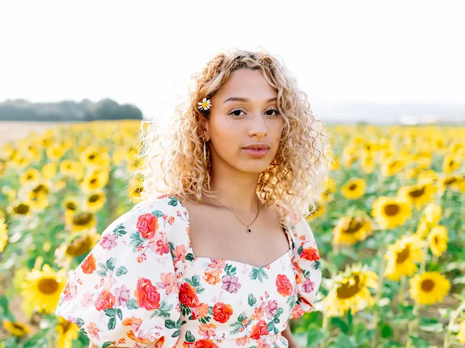Dame med fargerik blomsterkjole står i blomstereng 