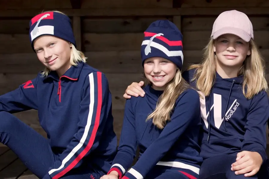 3 barn med blått, rødt ogh hvitt ulltøy som sitter på en benk.