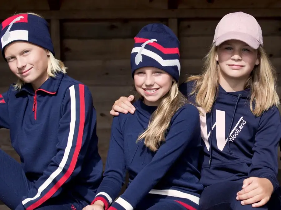 3 barn med blått, rødt ogh hvitt ulltøy som sitter på en benk.