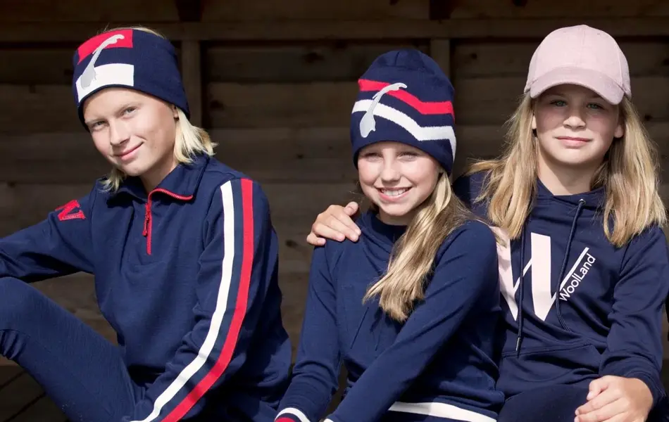 3 barn med blått, rødt ogh hvitt ulltøy som sitter på en benk.