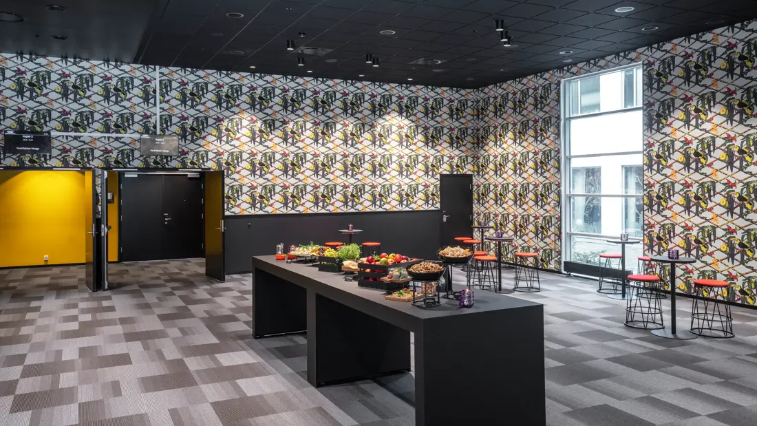 Oppholdsrom med barbenker, bord og stoler, mørkere gulv og mørkere vegger. 