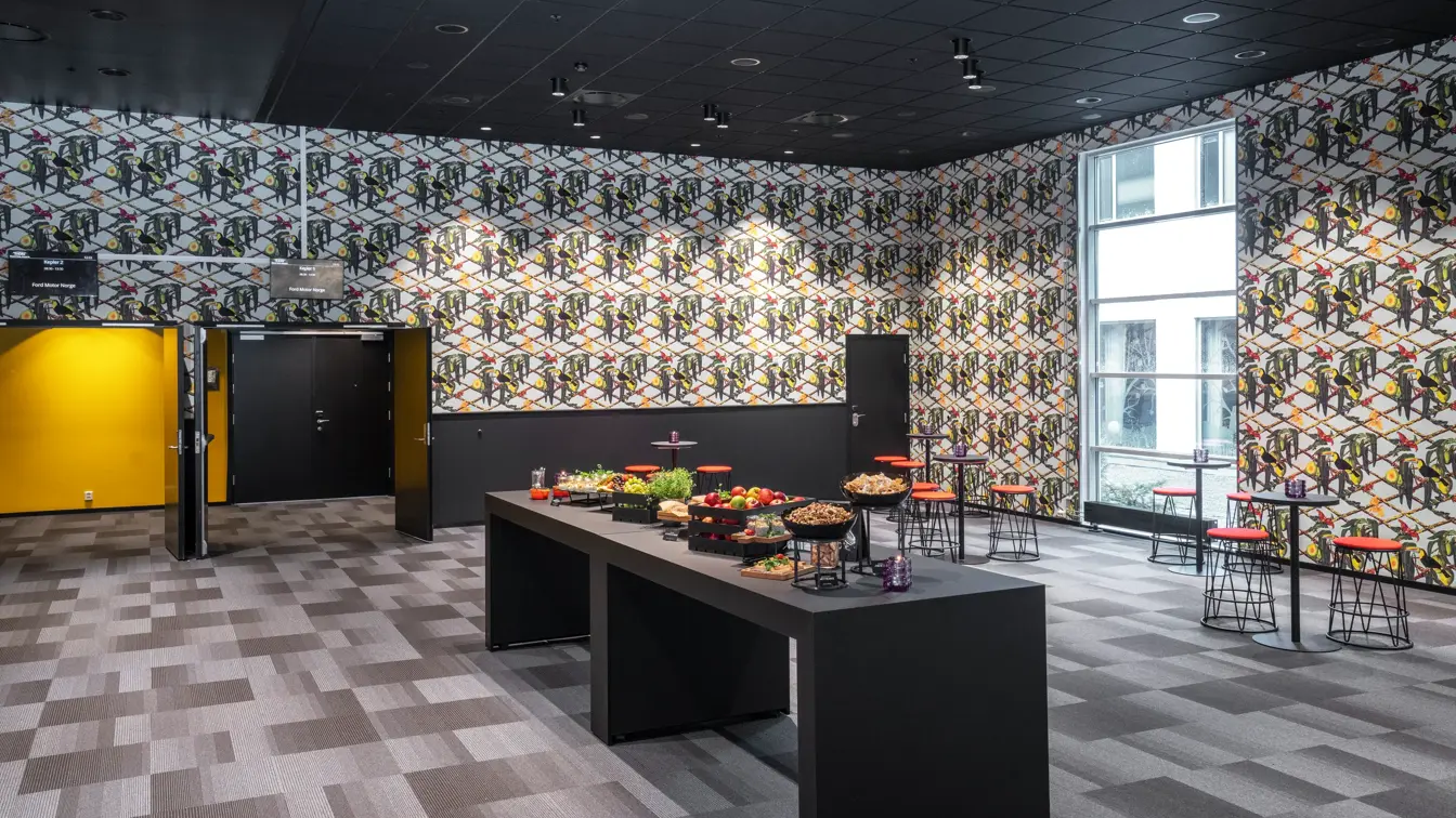 Oppholdsrom med barbenker, bord og stoler, mørkere gulv og mørkere vegger. 