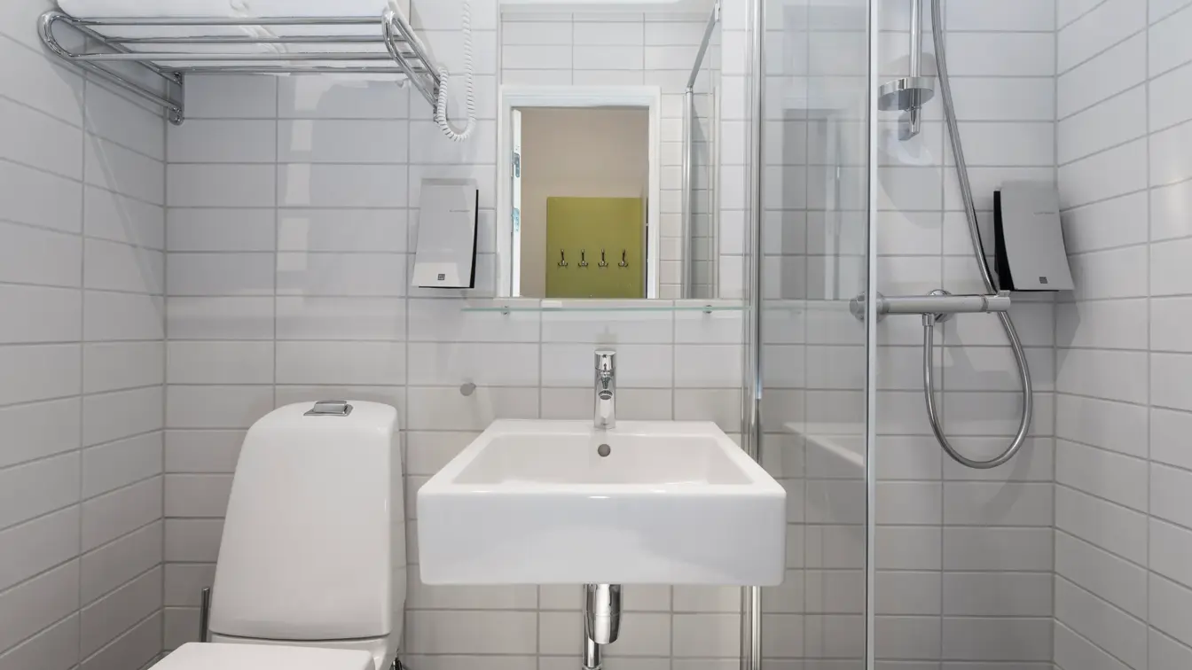 Standard bad på Thon Hotel Trondheim. Hvit innredning. Grå fliser på gulvet. Badet inneholder dusj, servant, speil og toalett.
