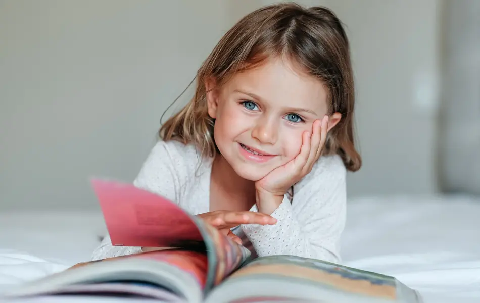 Happy girl kid lies on bed, read the book. Comfort, cozy home concept. Education develop child toddler