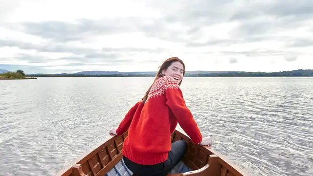 Dame med rød ullgenser sitter i båt og smiler til kamera