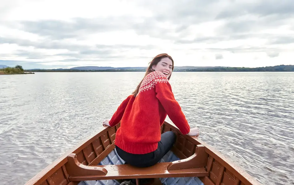Dame med rød ullgenser sitter i båt og smiler til kamera
