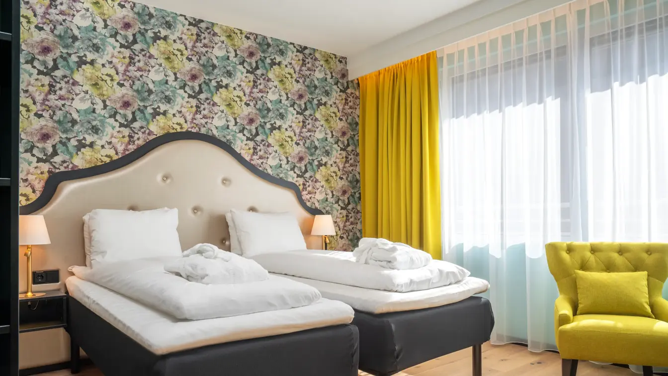 Separate senger med morgenkåper, blomstrete tapet, gule gardiner og store vinduer, gul stol i superior rom på Thon Hotel Cecil.