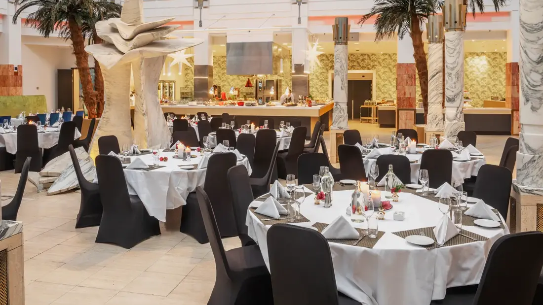 Runde oppdekede bord, palmer, åpent lokale, høyt under taket, svarte stoler