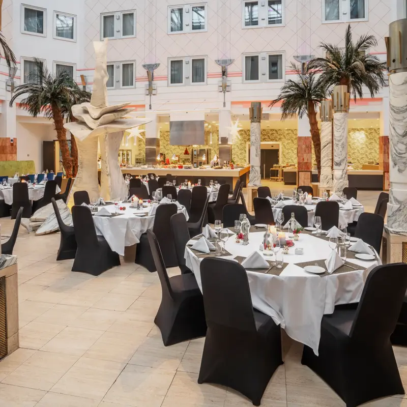 Runde oppdekede bord, palmer, åpent lokale, høyt under taket, svarte stoler