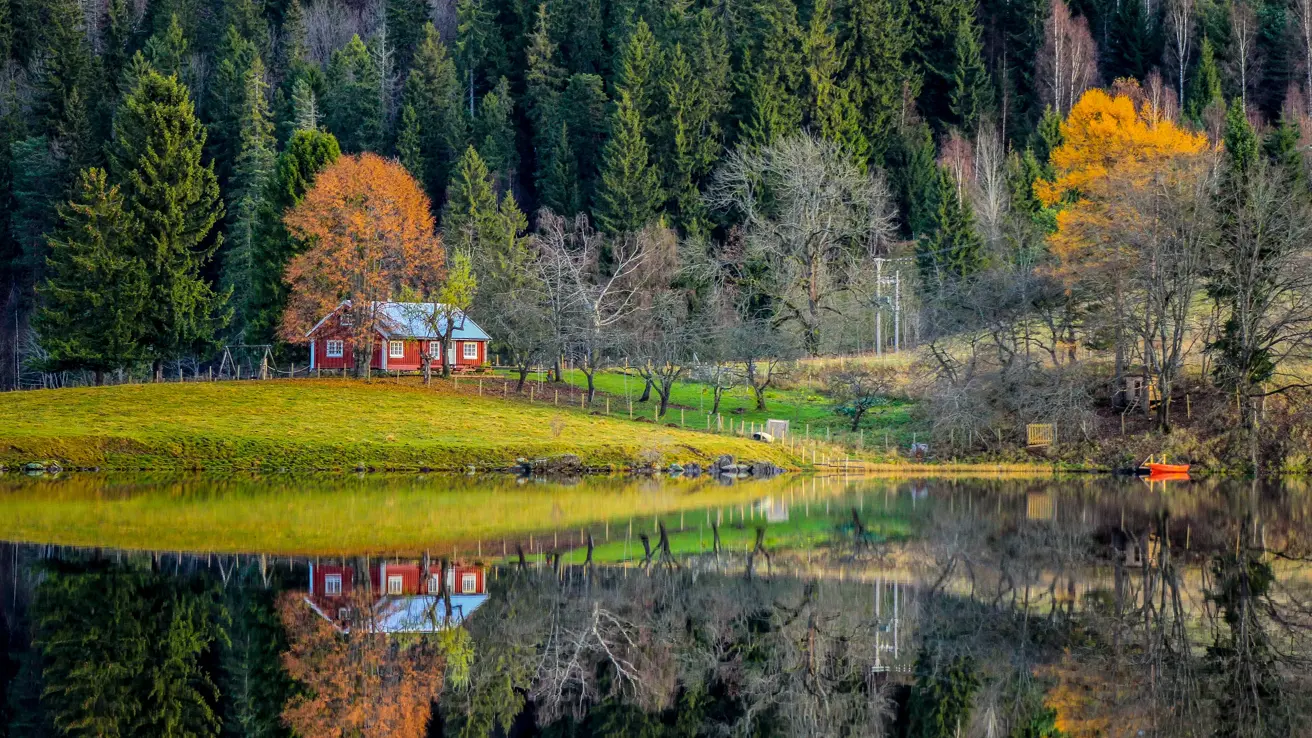 Semsvann i Asker. En rød hytte, med huskestativ utenfor. I forgrunnen ses vann. i bakgrunn skog i høstfarger.