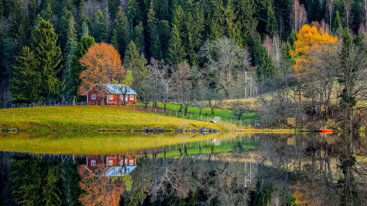 Semsvann i Asker. En rød hytte, med huskestativ utenfor. I forgrunnen ses vann. i bakgrunn skog i høstfarger.