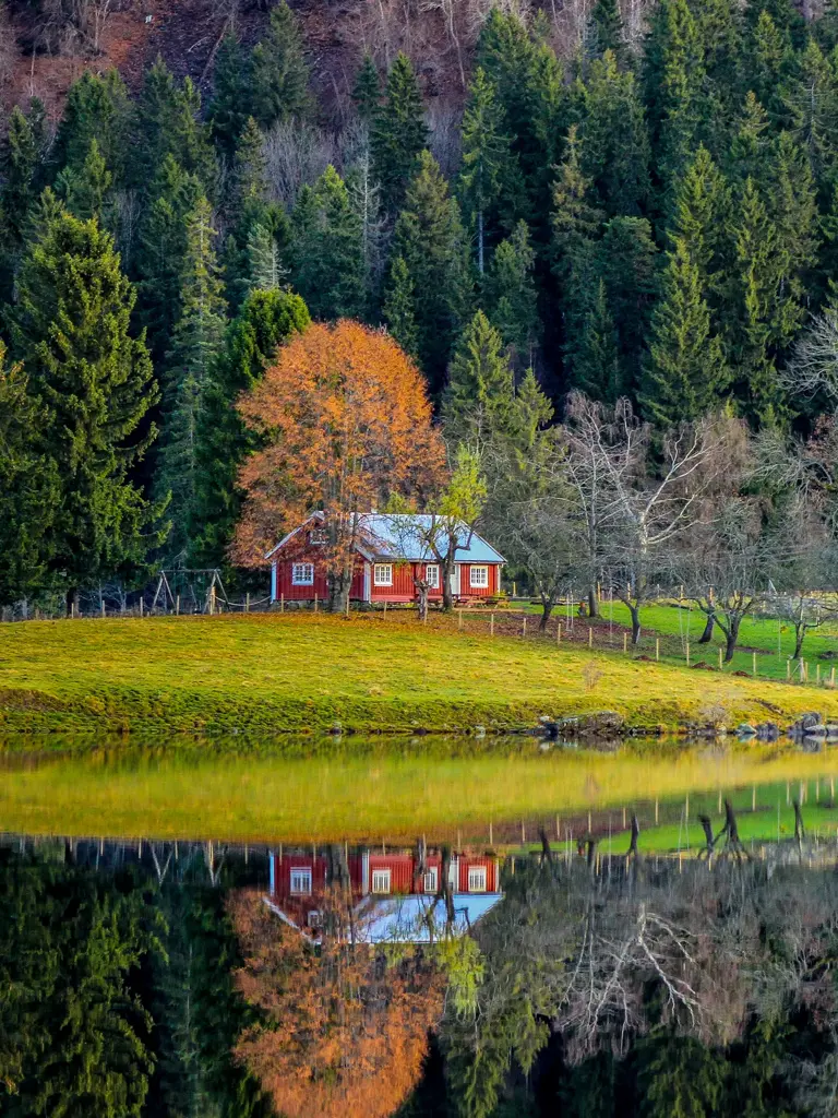 Semsvann i Asker. En rød hytte, med huskestativ utenfor. I forgrunnen ses vann. i bakgrunn skog i høstfarger.