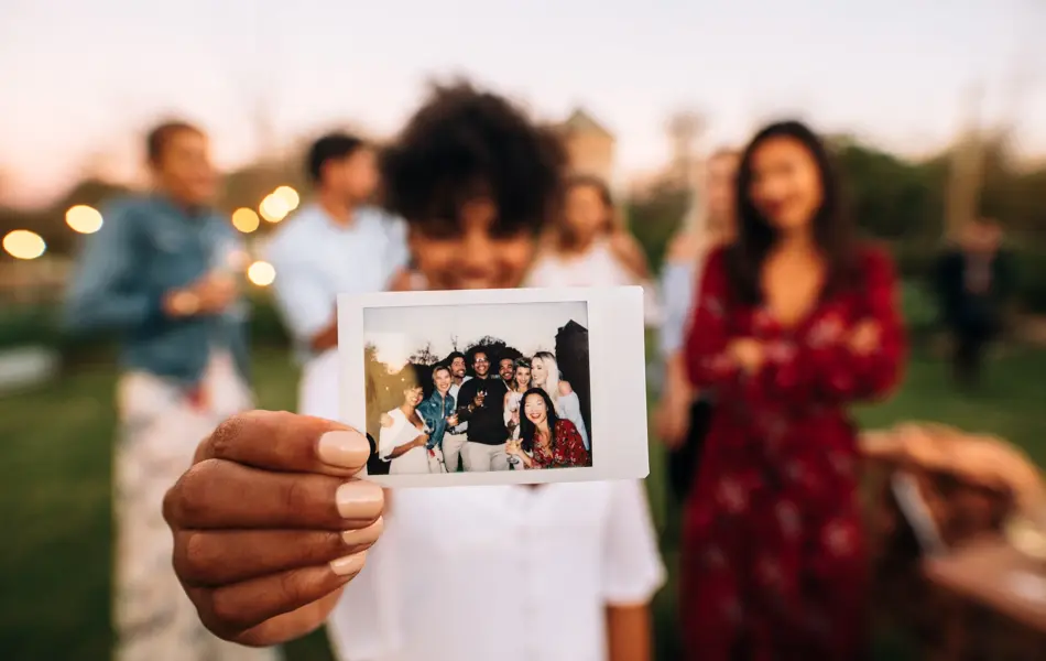 Woman showing picture in front with friends partying in background. Group photo of party people.