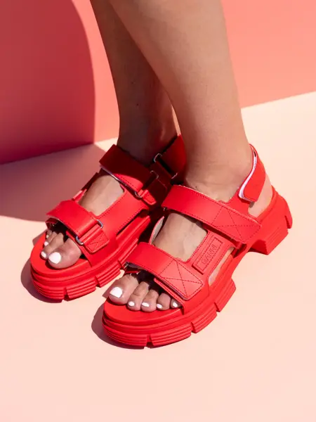 Røde grove sandaler på bare føtter med ferskenfarget bakgrunn