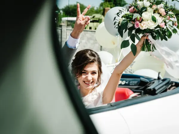 A newlywed wedding couple is driving a convertible retro car with balloons on a country straight road for their honeymoon. Way near spring field of flowers. The best day and marriage. Just married.