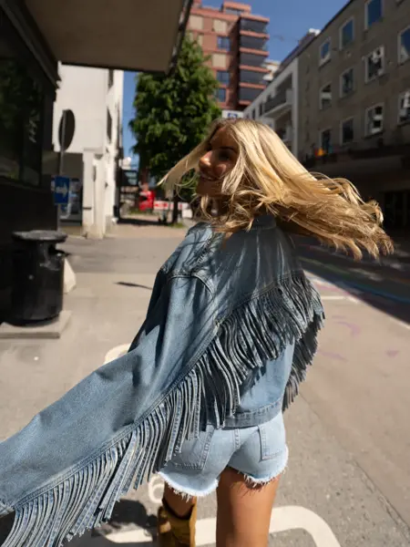 Jente går ute med olajakke med frynser og kort olashorts