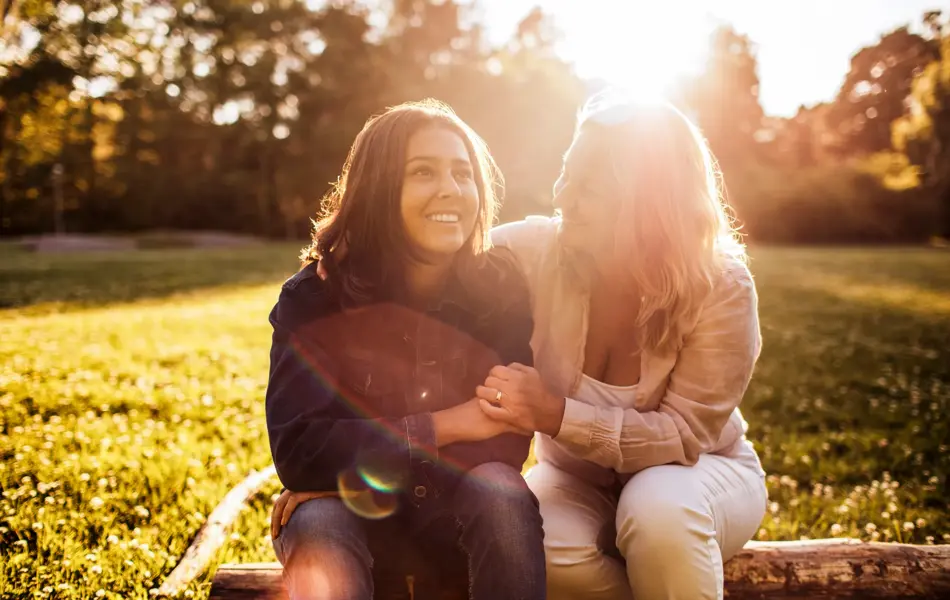 Mor og datter sitter ute på benk med solnedgang