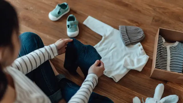 High angle shot of pregnant woman unpacking parcel of baby clothing from online shopping. Baby goods laying on the floor. Getting ready for a new born!