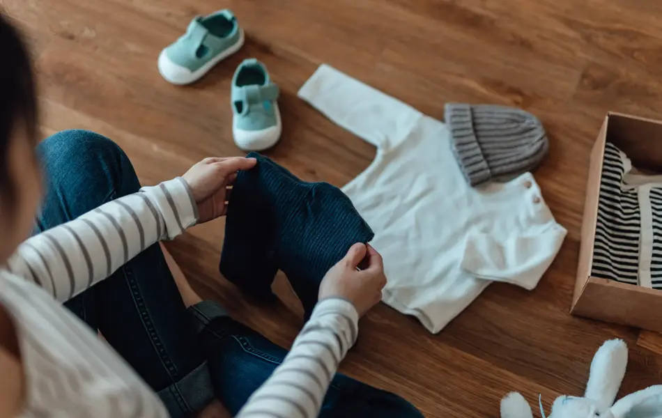 High angle shot of pregnant woman unpacking parcel of baby clothing from online shopping. Baby goods laying on the floor. Getting ready for a new born!