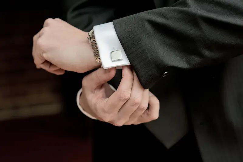 Nærbilde av hender, skjorteerme med mansjettknapp og sort dressjakke