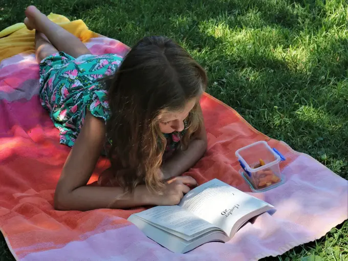Jente som leser bok ute i hagen