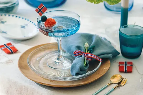 Kuvert med tretallerken, glasstallerken og coctailglass. Blått vannglass og flaggpynt.